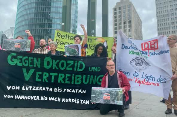 Un grupo de personas protesta con grandes pancartas de varias organizaciones, delante de unos edificios