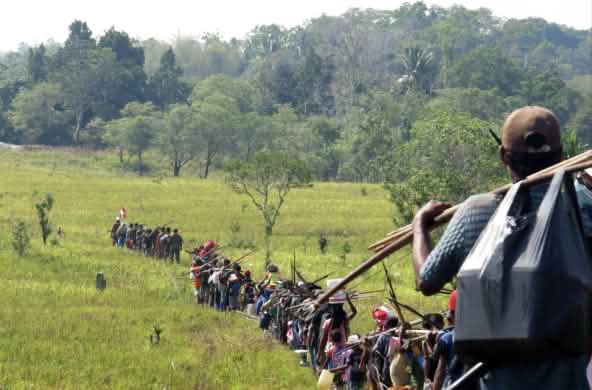 Indígenas en fila atraviesan una sabana para ir a cazar