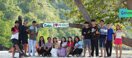 Un grupo de jóvenes de la organización Mother Nature Camboya sentados y de pie frente a un árbol en la playa