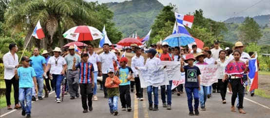 Manifestantes marchan con pancartas, banderas nacionales y paraguas por una carretera en Panamá