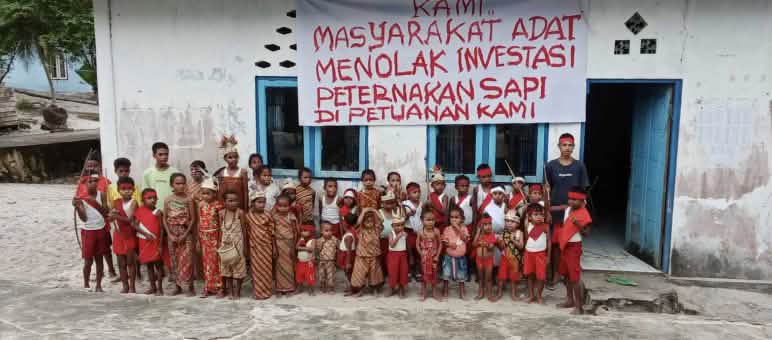 «¡Rechazamos las inversiones en ganadería bovina en nuestras tierras ancestrales!» Grupo de niños delante de una escuela en la que cuelga una pancarta con un mensaje en indonesio