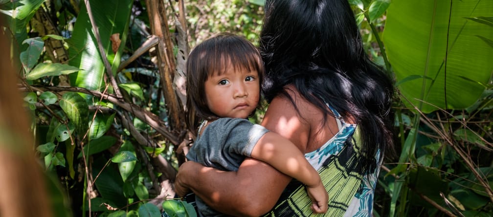 La vida de los pueblos indígenas depende de la salud del medio Mujer indígena ka'apor entre la vegetación de la selva amazónica con su hijo en brazos