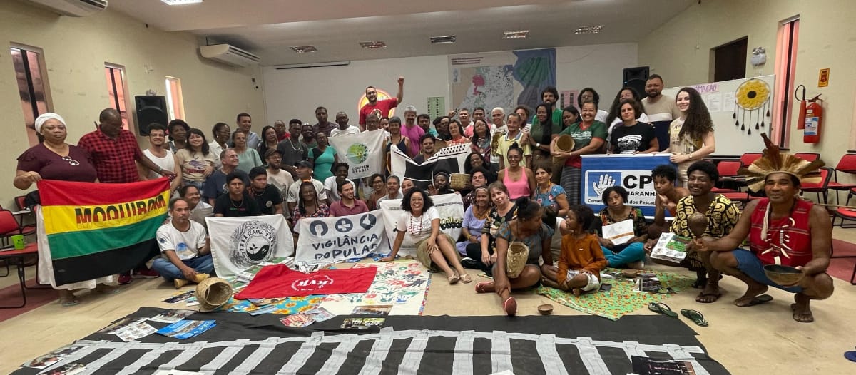 Foto de grupo de cerca de 50 personas con pancartas en una sala de reuniones