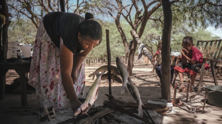 Mujer asando pescado bajo la atenta mirada de dos niños