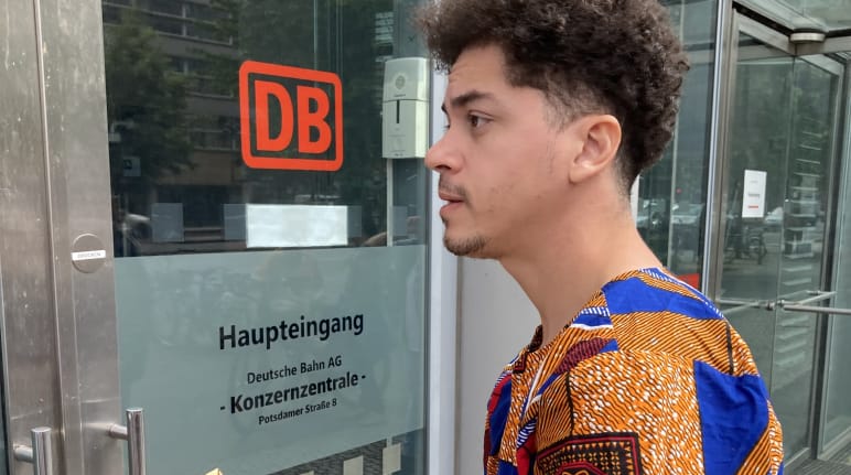 Una persona con un sobre, delante de la entrada de la sede principal de la empresa Deutsche Bahn DB