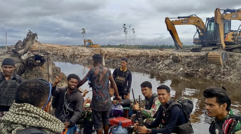 Grupo de hombres con excavadoras mecánicas al fondo frente a un paisaje devastado