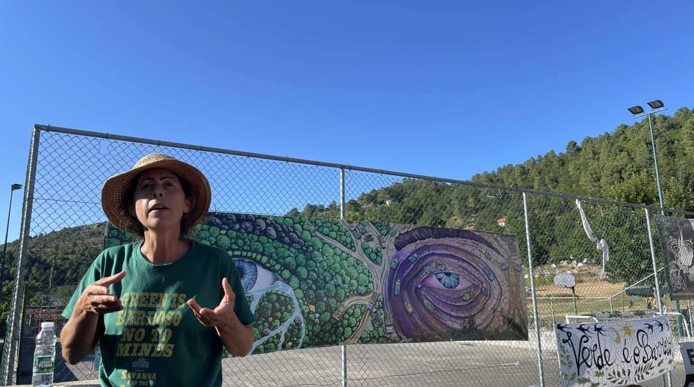 Aida Fernandes  de Covas do Barroso con una camiseta con la leyenda "Green is Barroso, No to the Mines", al fondo una pancarta que marca el contraste entre la minería y la naturaleza íntegra